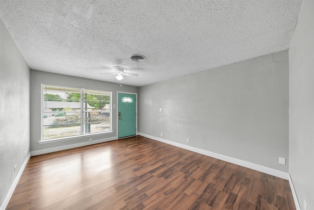 empty room with a textured ceiling, a ceiling fan, baseboards, wood finished floors, and visible vents