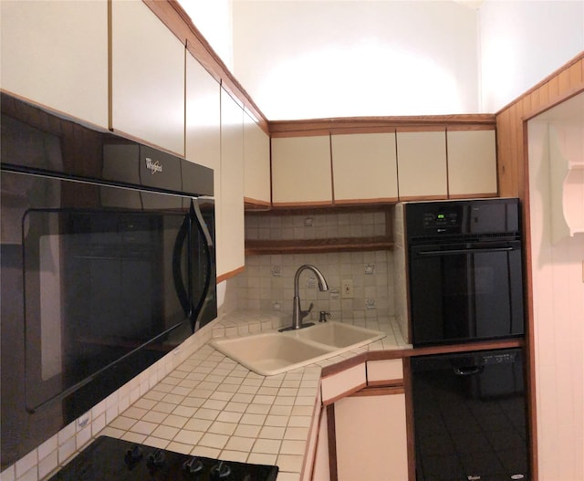 kitchen with decorative backsplash, tile counters, white cabinets, a sink, and black appliances