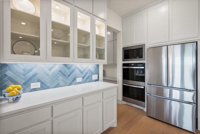 kitchen with backsplash, appliances with stainless steel finishes, light countertops, white cabinets, and glass insert cabinets
