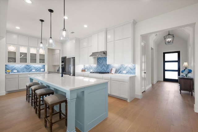kitchen featuring decorative backsplash, a kitchen bar, light countertops, under cabinet range hood, and appliances with stainless steel finishes