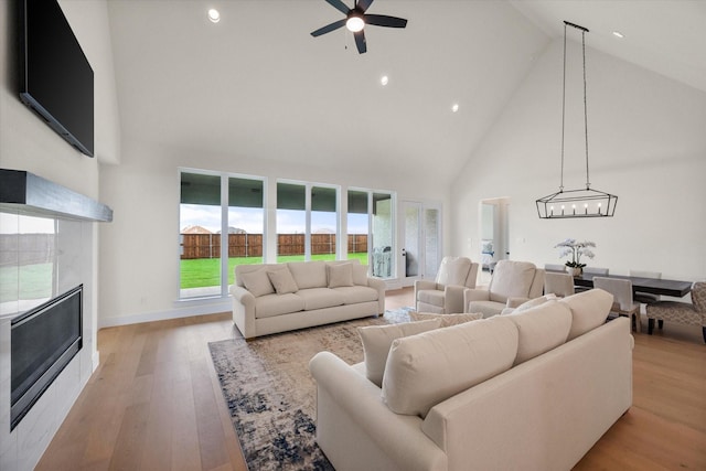 living area with high vaulted ceiling, ceiling fan with notable chandelier, recessed lighting, and a tile fireplace