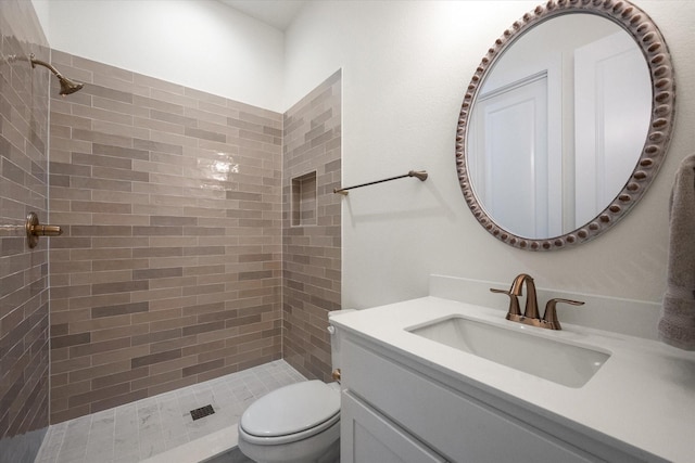 bathroom with toilet, a tile shower, and vanity