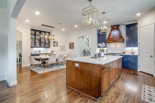 kitchen featuring decorative backsplash, a kitchen island, glass insert cabinets, custom range hood, and arched walkways