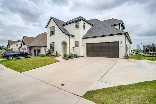 french country home with roof with shingles, a garage, fence, a front lawn, and concrete driveway