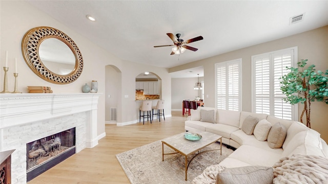 living area featuring a ceiling fan, light wood-style floors, visible vents, and arched walkways
