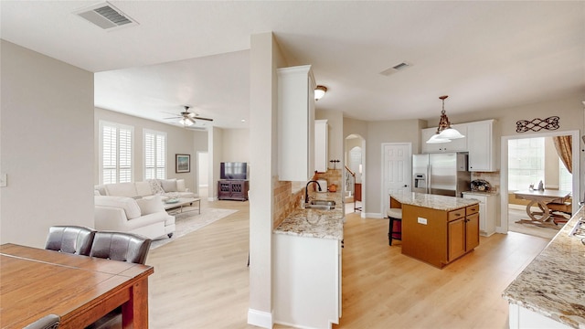 kitchen with visible vents, a sink, stainless steel refrigerator with ice dispenser, arched walkways, and light wood-style floors