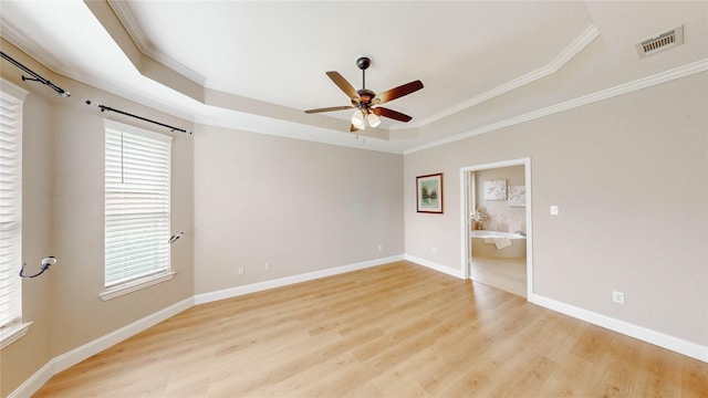 empty room with a raised ceiling, ceiling fan, visible vents, and a wealth of natural light