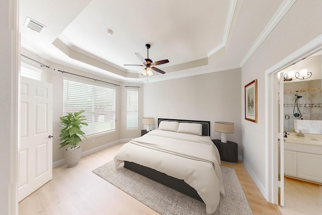 bedroom with a raised ceiling, light wood-type flooring, ensuite bathroom, ornamental molding, and ceiling fan