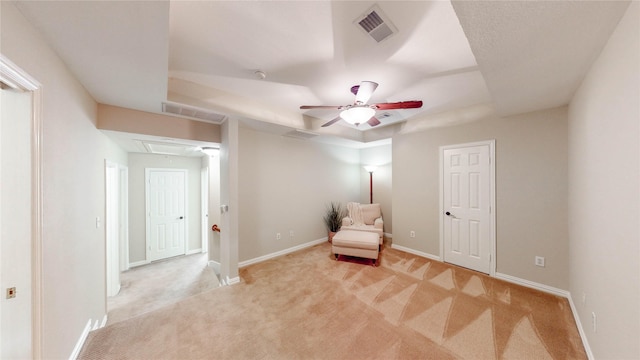 unfurnished room with a raised ceiling, attic access, a ceiling fan, and visible vents