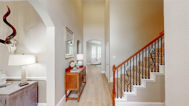interior space featuring arched walkways, baseboards, a towering ceiling, and wood finished floors