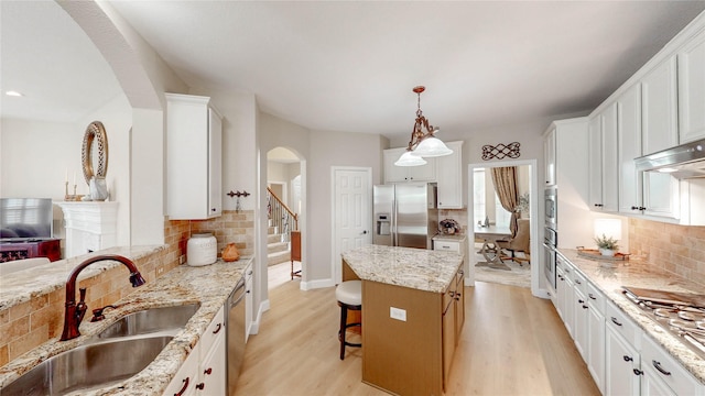 kitchen featuring a sink, decorative backsplash, arched walkways, and appliances with stainless steel finishes