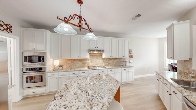 kitchen with light wood-style flooring, stainless steel appliances, visible vents, backsplash, and under cabinet range hood