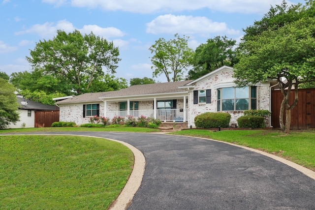 ranch-style house with brick siding, a front lawn, fence, and covered porch