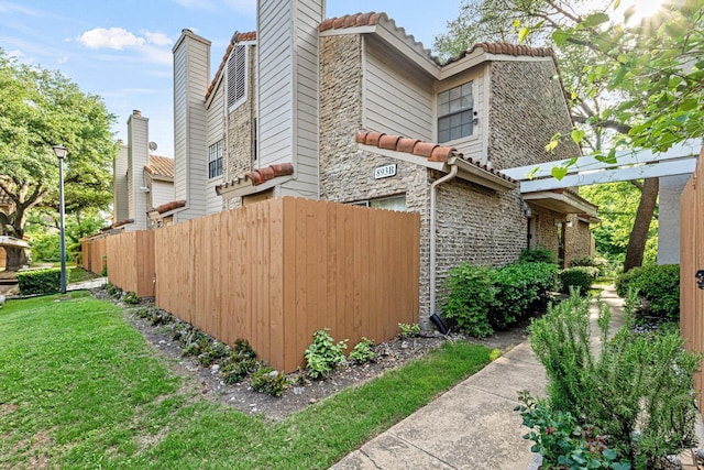 view of home's exterior featuring a chimney, fence, a tile roof, and stone siding