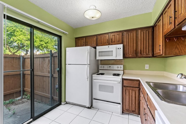 kitchen with a textured ceiling, a sink, light countertops, white appliances, and light tile patterned flooring