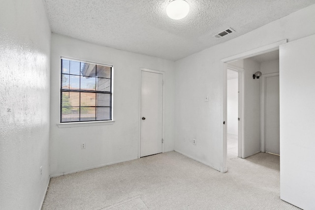 spare room featuring a textured ceiling, visible vents, and light carpet