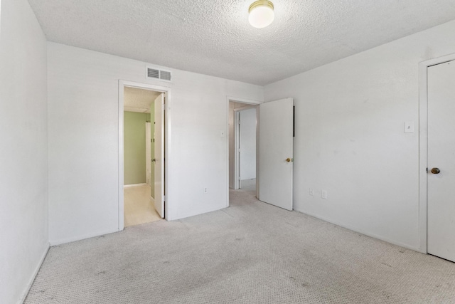 unfurnished bedroom with carpet, ensuite bath, a textured ceiling, and visible vents