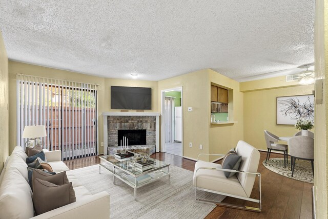living room with a brick fireplace, a textured ceiling, a ceiling fan, baseboards, and hardwood / wood-style flooring