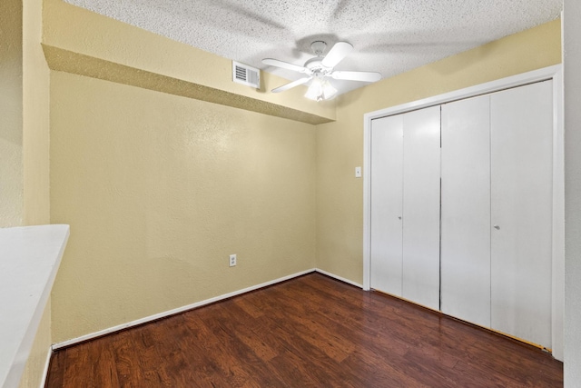 unfurnished bedroom with ceiling fan, a textured wall, dark wood-type flooring, visible vents, and a closet