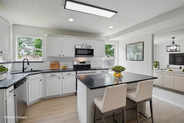 kitchen featuring backsplash, a textured ceiling, a sink, light wood-style floors, and stainless steel appliances