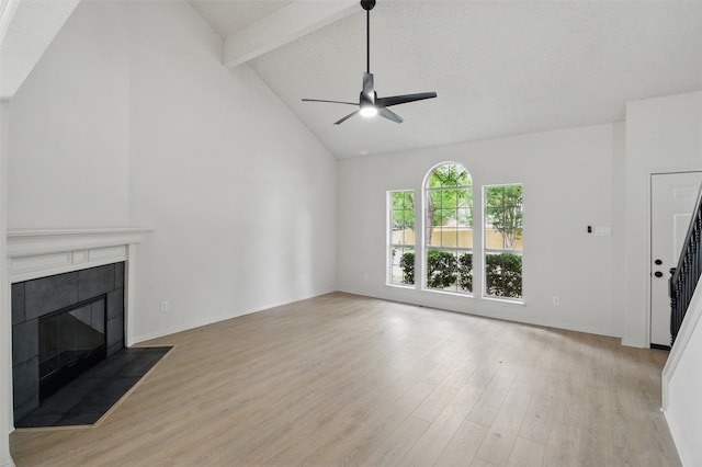 unfurnished living room with ceiling fan, a tile fireplace, beam ceiling, and light wood-type flooring