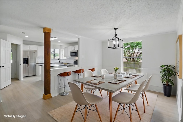 dining space featuring light wood finished floors, a textured ceiling, and a chandelier