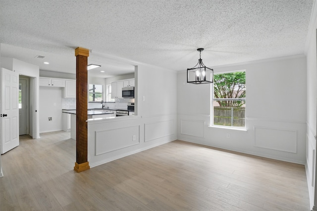 unfurnished dining area featuring a notable chandelier, a textured ceiling, a sink, and light wood-style flooring