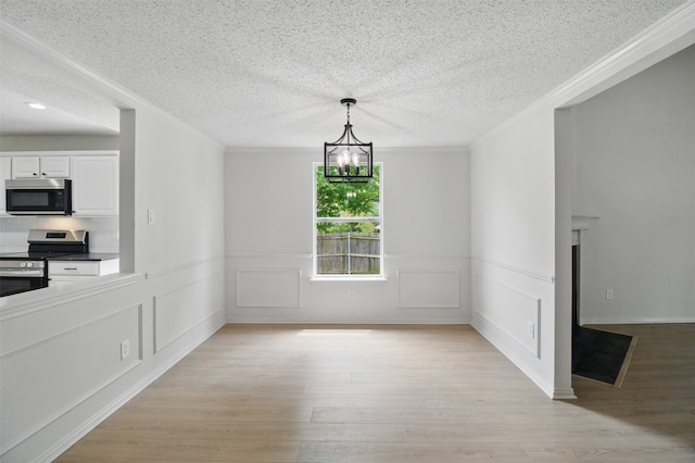 unfurnished dining area with crown molding, a textured ceiling, a notable chandelier, and light wood-style flooring