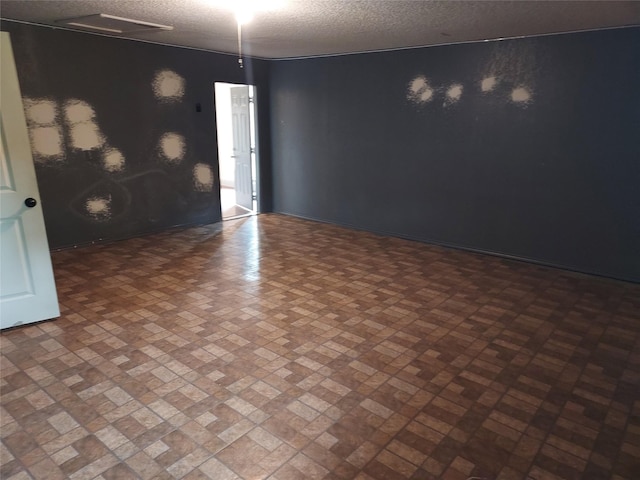 empty room featuring a textured ceiling, brick patterned floor, and baseboards