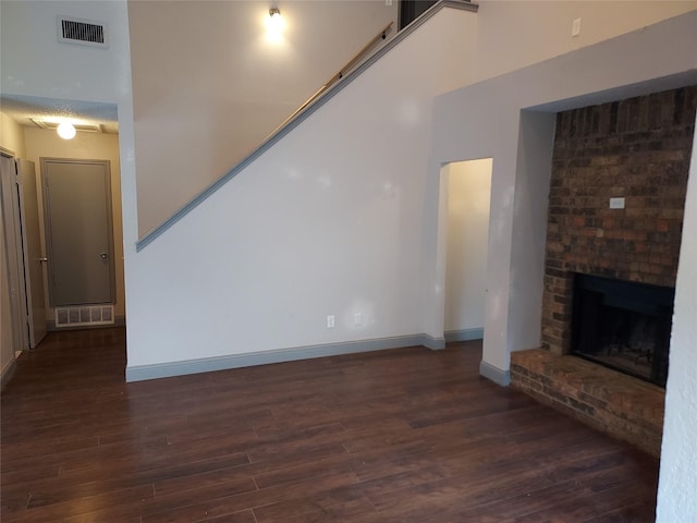unfurnished living room with baseboards, a brick fireplace, wood finished floors, and visible vents