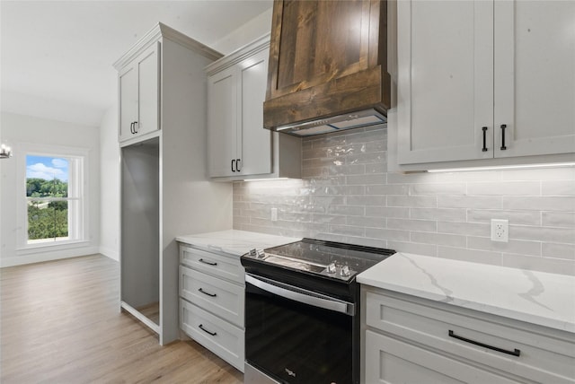 kitchen featuring backsplash, electric range, light stone countertops, light wood-style floors, and custom range hood