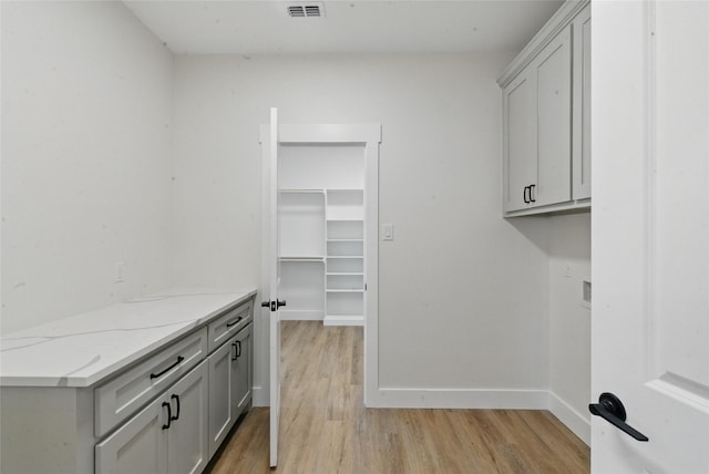 washroom with cabinet space, baseboards, visible vents, and light wood-style floors
