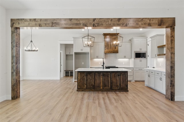 kitchen with a notable chandelier, light wood-style floors, light countertops, stainless steel microwave, and tasteful backsplash