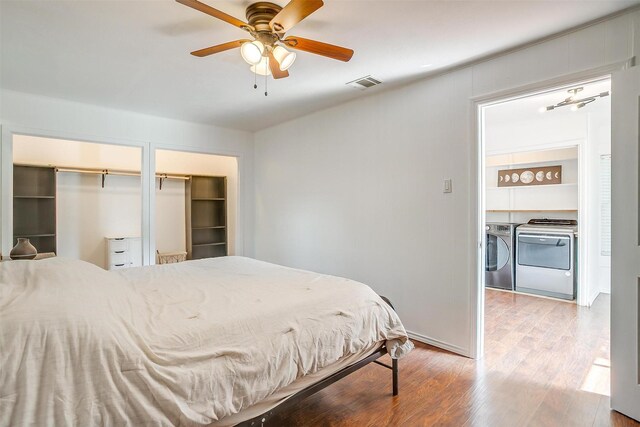 bedroom featuring visible vents, wood finished floors, two closets, washing machine and clothes dryer, and a ceiling fan