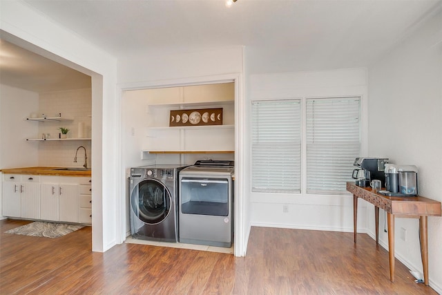 clothes washing area featuring washing machine and clothes dryer, laundry area, a sink, and wood finished floors
