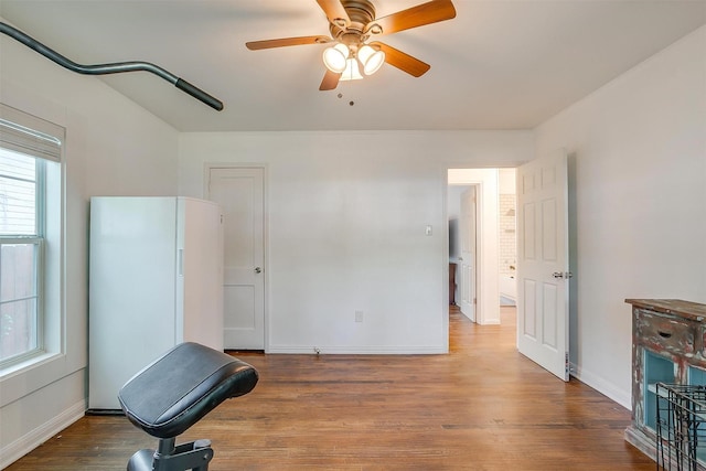 unfurnished bedroom with baseboards, ceiling fan, freestanding refrigerator, and wood finished floors