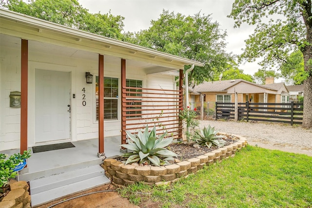 view of exterior entry featuring a porch and fence