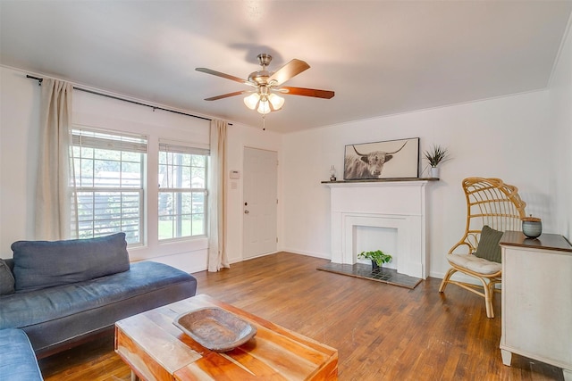 living room featuring baseboards, a fireplace with raised hearth, ceiling fan, and wood finished floors