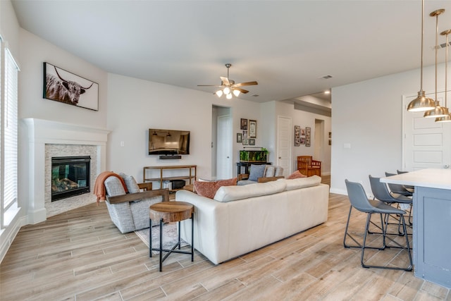 living room featuring a ceiling fan, a stone fireplace, visible vents, light wood-type flooring, and baseboards