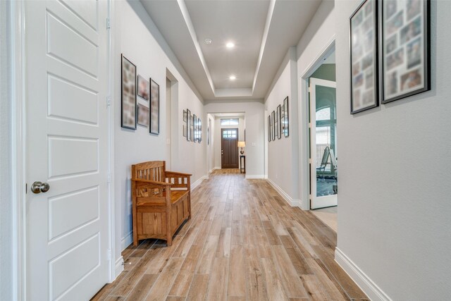hallway featuring recessed lighting, baseboards, light wood-style flooring, and a tray ceiling