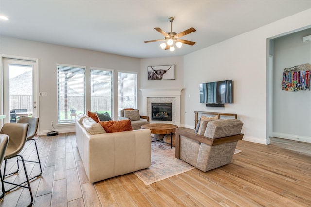 living room featuring a ceiling fan, baseboards, a glass covered fireplace, and light wood-style floors
