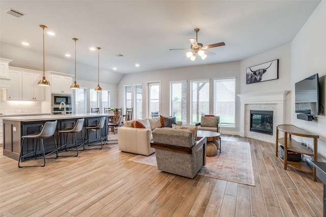living room featuring a fireplace, light wood-style flooring, a ceiling fan, vaulted ceiling, and visible vents