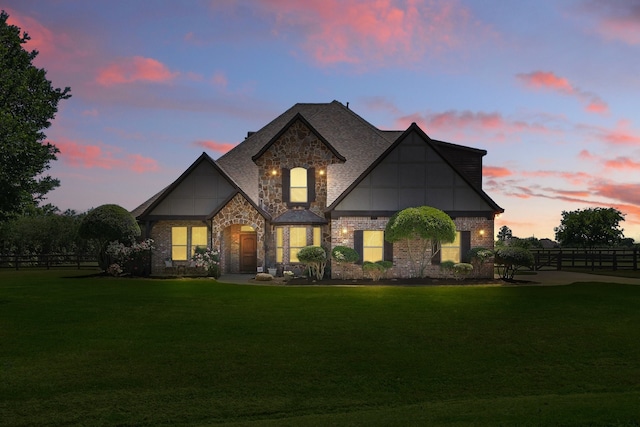 view of front facade featuring a lawn, brick siding, fence, and stone siding