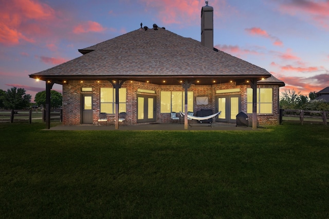 back of house at dusk featuring brick siding, a yard, french doors, and a patio