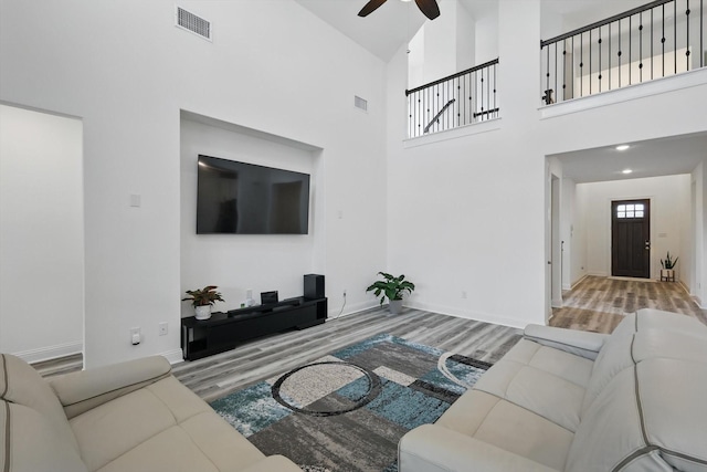 living room featuring a ceiling fan, a high ceiling, visible vents, and wood finished floors