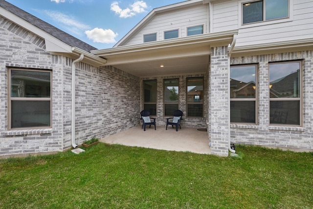 rear view of house with a patio, a yard, and brick siding