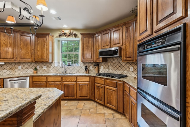 kitchen featuring brown cabinets, light stone countertops, a sink, stainless steel appliances, and visible vents