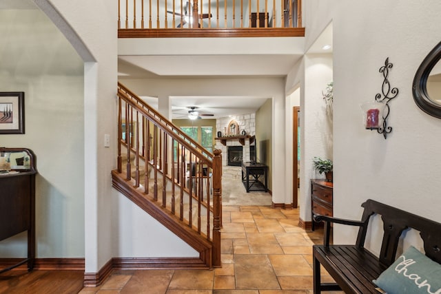foyer featuring ceiling fan, a stone fireplace, arched walkways, baseboards, and stone tile floors