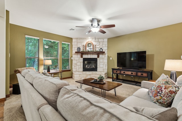 living room featuring ceiling fan, visible vents, a stone fireplace, and baseboards