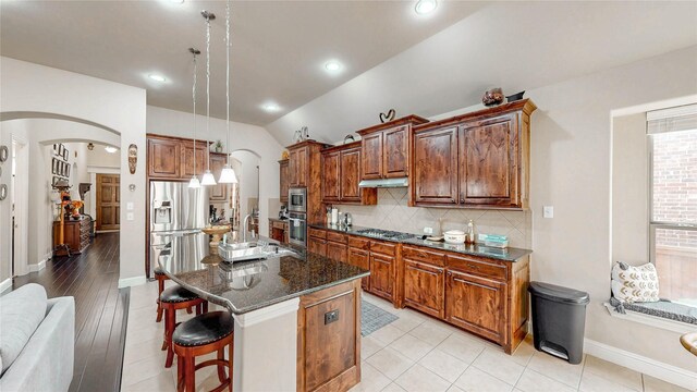 kitchen featuring a sink, lofted ceiling, a breakfast bar area, arched walkways, and backsplash